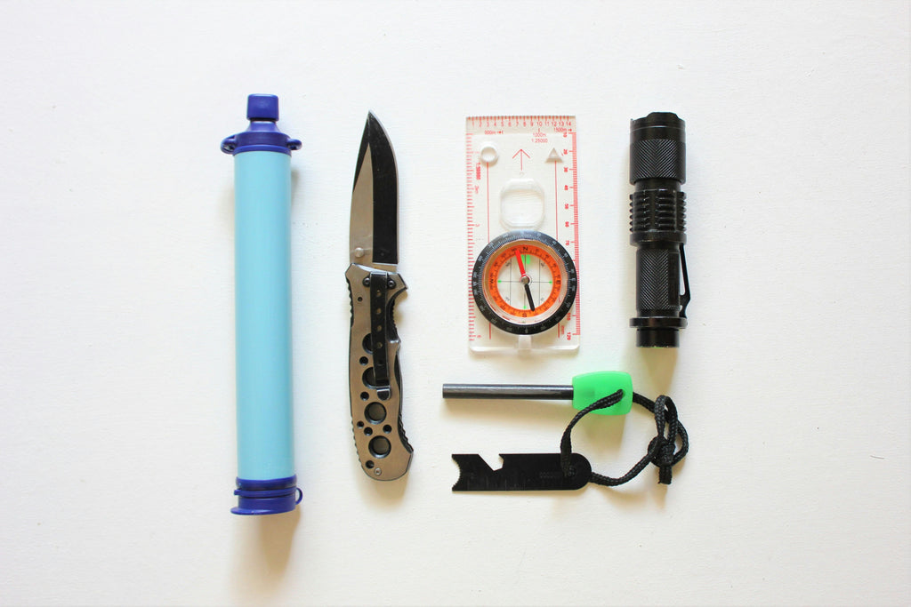 A few items used for outdoor adventure and survival including water filtering straw, knife, and compass.